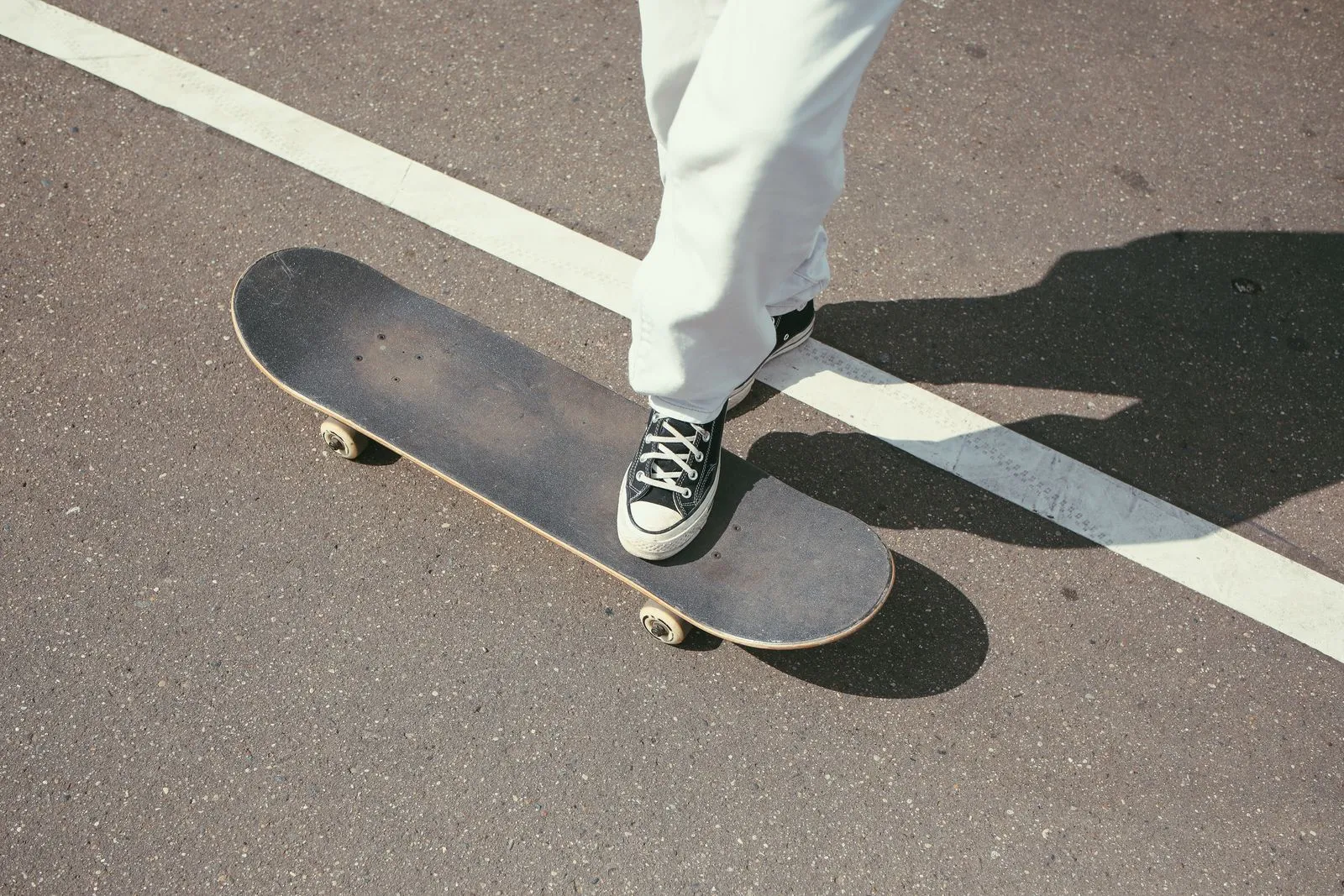 Skateboarder's foot balancing on board on sunny street pavement.